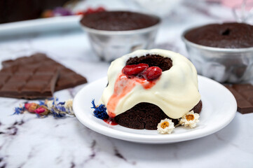 Rectangular and round chocolate pudding with cream on top and strawberries on a table with ingredients and pastry chef's hands decorating