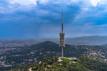 View of the Torre de Collserola television tower on top of Tibidabo hill in amusement park in summer, with Mediterranean sea in background, Barcelona, Spain