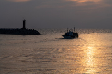 fishing boat and lighthouse at the harbor during sunset