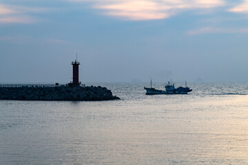 Fototapeta premium fishing boat and lighthouse at the harbor during sunset