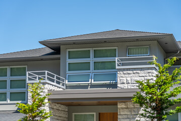 Top of grey stucco luxury house with shingle roof, green trees and nice windows in Spring in Vancouver, Canada, North America. Day time on May 2025.