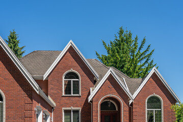 Top of grey stucco luxury house with shingle roof, green trees and nice windows in Spring in Vancouver, Canada, North America. Day time on May 2025.