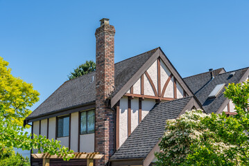 Top of grey stucco luxury house with shingle roof, green trees and nice windows in Spring in Vancouver, Canada, North America. Day time on May 2025.
