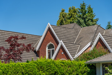 Top of grey stucco luxury house with shingle roof, green trees and nice windows in Spring in...