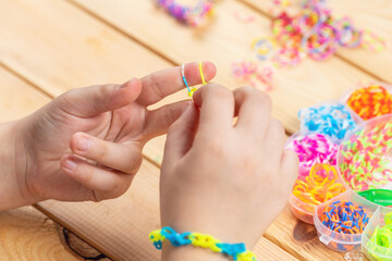 The child's hands weave accessories from colorful rubber bands. Children's hobby
