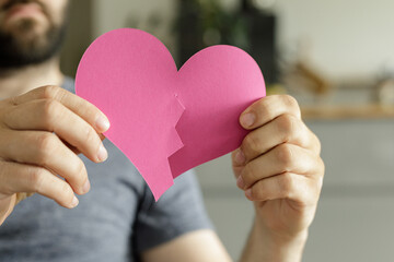 A man holds a broken pink paper heart, symbolizing heartbreak, sadness, and relationship problems.
