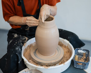 Close-up of a potter's hands making a ceramic vase on a potter's wheel. 