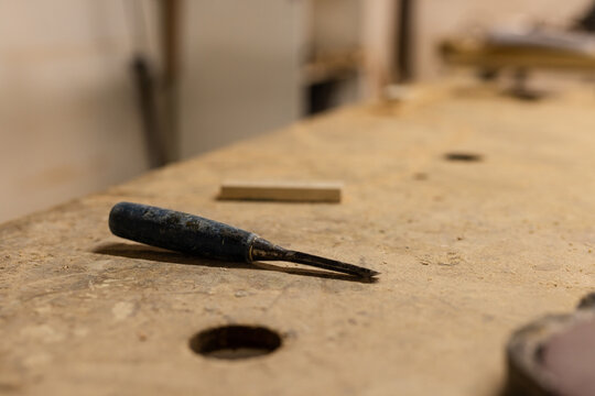 Metal-bladed chisel resting near drilled hole on sawdust strewn carpentry bench with wood shavings