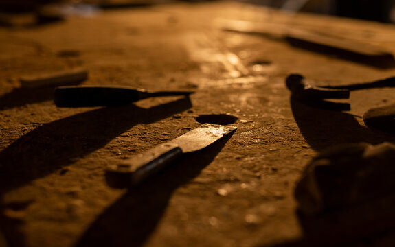 Putty knife resting on workbench under warm light, with scraper blades and hammer handle