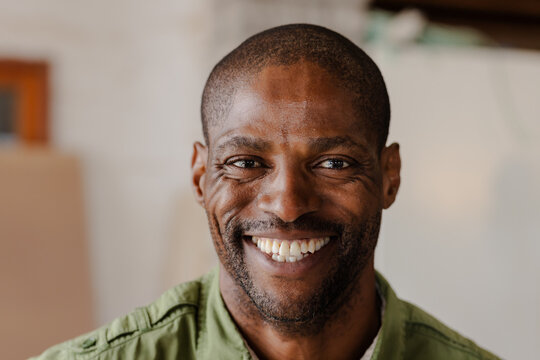 African American man smiling warmly at camera in living area wearing green button-up shirt