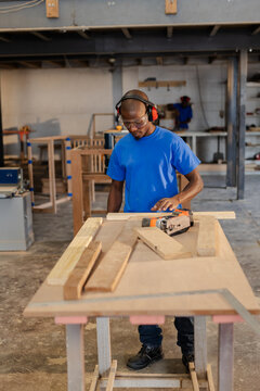 Central workbench holding wooden planks, nail gun, metal square in workshop with shelves