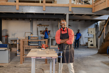 African American male coworkers working at workbench using red electric sander and clamps in shop