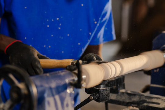 African American man operating wood lathe machine with chisel in workshop, shaping wooden spindle