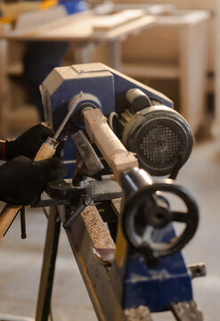 Wood lathe rotating wooden blank in workshop, with gloved hands carving fine wood shavings