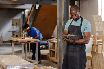 African American coworkers working in workshop using tablet and sander near drill press, copy space