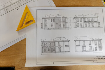 House elevation blueprint sheet lying on wooden desk in office, with yellow triangular ruler