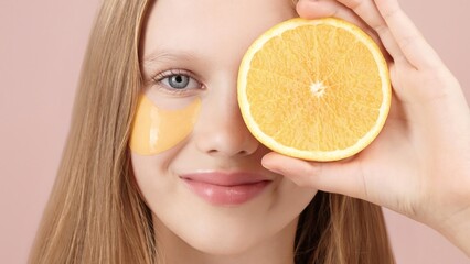 Happy cute young girl with eye patch on studio pink background. Orange. Cute portrait of blonde girl gen Alpha smiling looking at the camera. Concept of cosmetics advertisement for teenagers. Skincare