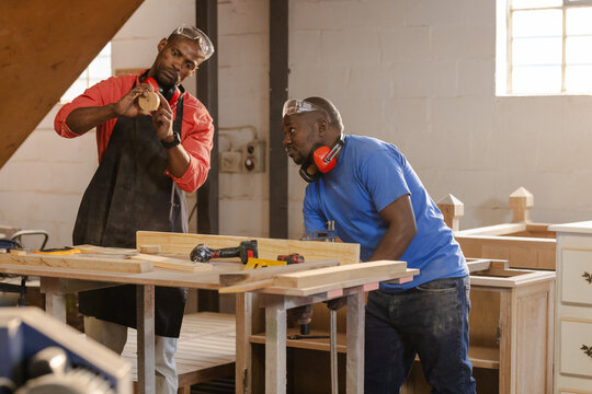 African American male carpenters examining circular cutout at workshop bench with power tools
