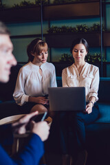 Female executives in formal wear analyzing program on laptop together at lobby of business center