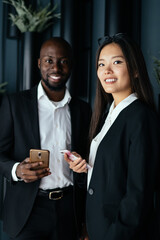 Multiracial confident business people using smartphones before meeting in modern office