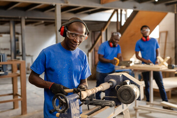 African American male coworkers operating wood lathe and sanding planks at carpentry workshop