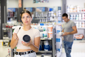 In store, female buyer doubt choice and examines product, paint jar studies detailed information on...