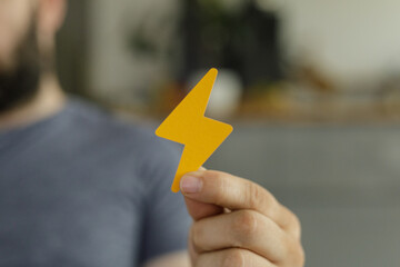 Close-up of a hand holding a yellow lightning bolt cutout. Represents speed, energy, power.