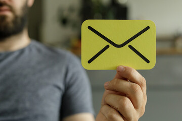 Close-up of a man holding a yellow card with an email icon.  Concept for email, message,...