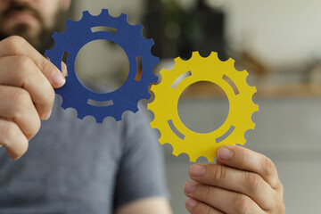 Image of hands holding blue and yellow gears, symbolizing teamwork, collaboration, and synergy.