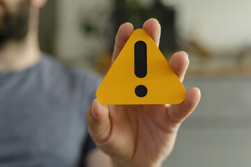 Close-up of a person's hand holding a yellow triangle with an exclamation mark, signifying warning or alert.
