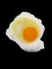 A sunny side up egg with a vibrantly colored orange yolk, on a black background. 