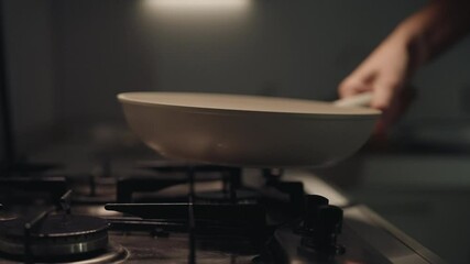Professional chef placing skillet on gas stove in dark restaurant kitchen, heating up sunflower oil, preparing to create delicious meal filled with rich flavors and aromas, close-up, slow motion.