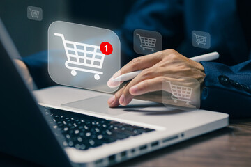Online shopping concept showing a hand using a laptop and stylus with a digital shopping cart icon and notification for an e-commerce purchase.