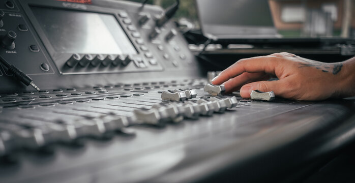 the hand of a tattooed person controlling a sound mixer at a live event