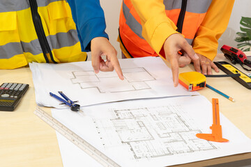 Two construction workers in safety vests review architectural blueprints