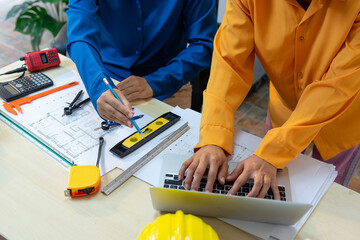 Two engineers collaborate on project with blueprints and laptop