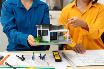 Two people discussing house model over architectural plans