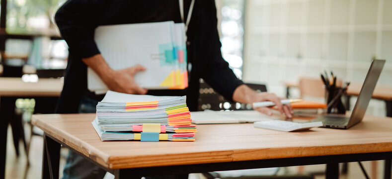 Portrait of an employee working with a large number of documents, searching for documents, accounting of income and expenses, tax records and checking documents on a desk in an office.