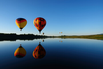 Obraz premium Hot air balloons floating in sky above lake at sunrise.