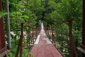 Old red wooden suspension bridge over the Chorukh River, Georgia