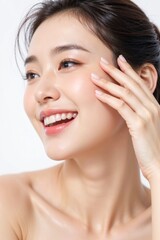 Beautiful young Korean woman smiling with radiant skin, touching her face gently, isolated on white background, showing natural beauty and happiness