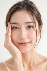 Beautiful young Thai woman with clear skin smiling hand touching face natural makeup isolated on white background healthy complexion relaxed expression brown hair close up portrait soft lighting
