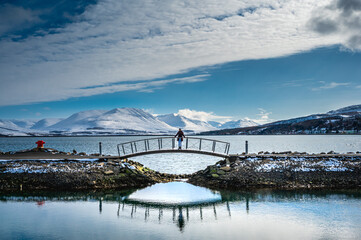 Fototapeta premium Woman standing in the middle of bridge looking at beautiful panoramic view of snowy mountain in Iceland