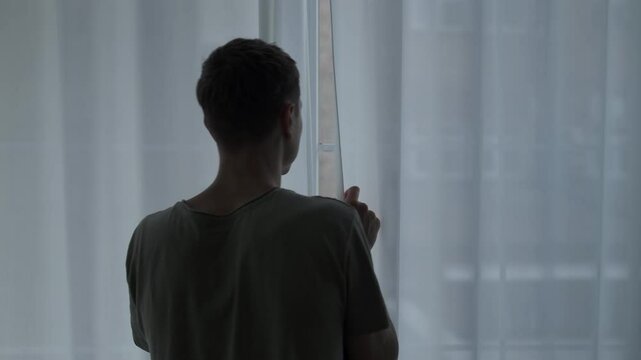 Man standing still by the window, struggling with social anxiety, panic disorder, and isolation syndrome.