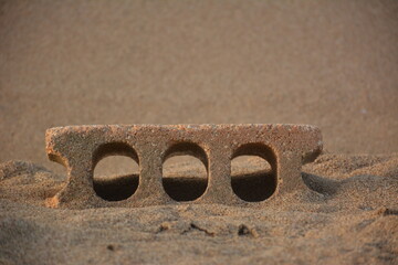 A tiny sandcastle brick sits neatly on the beach, its rough edges catching sunlight. Surrounding...