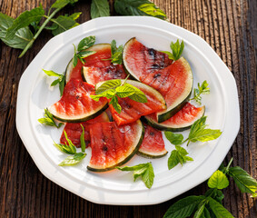 Grilled watermelon salad with addition fresh mint leaves on a white plate