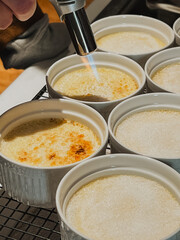 Torch Caramelizing Crème Brûlée Sugar Topping in White Ramekins, Close-Up of Classic French Dessert Preparation