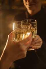 Close-up shot of two people clinking glasses of white wine in a warm, cozy atmosphere. Perfect for celebrating, socializing, or enjoying a special moment together