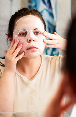 Female applying moisturizing face mask in bathroom. Beauty routine. International Self Care Day.