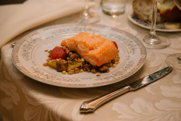 Salmon fillet served on a plate with grains and vegetables at a dining table during an elegant evening meal
